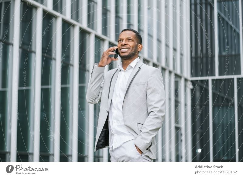 Elegant black man talking smartphone near building walking business architecture suit professional ethnic exterior african surfing corporate using futuristic