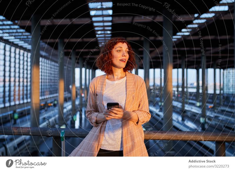 Smiling young woman holding phone at station railway smartphone call smile travel business vacation tourist communication terminal departure female suitcase