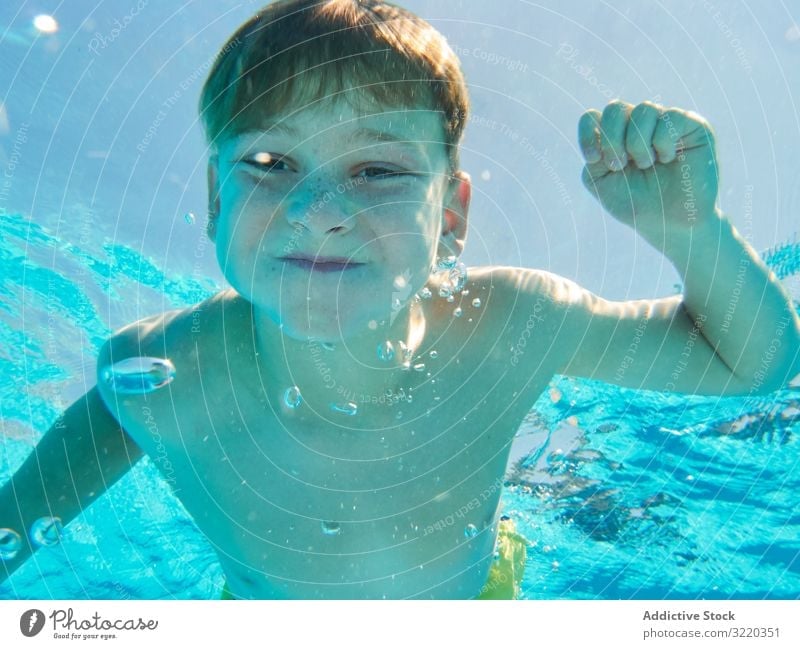 Funny boy swimming underwater looking at camera pool funny grimace breath hold child cheerful playful summer childhood dive swimwear vacation bubble recreation