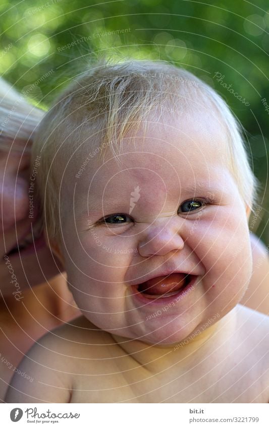 Little, sweet bundle of joy laughs, squeaking into the camera. Happy baby, toddler with mother laughs up to the ears, outside in the nature. Blonde girl in the swimming pool with happy facial expressions, facial expression. Light spots of the green meadow in the back.