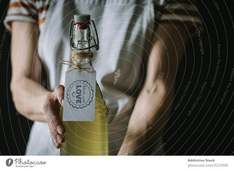 Female with bottle of elderflower syrup woman glass homemade beverage drink refreshment female casual serious striped t-shirt apron stand fruit cider lemon