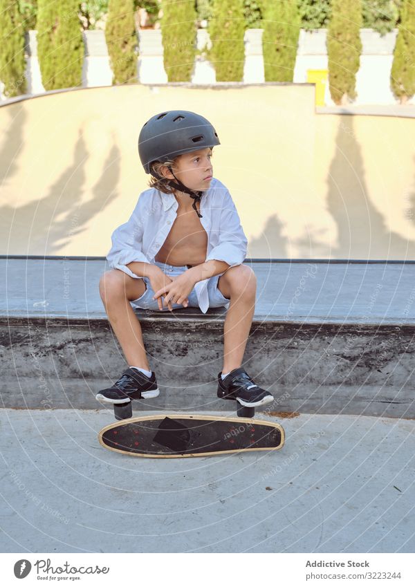 Boy with skateboard sitting on ramp boy skatepark helmet lifestyle sport leisure hobby male young childhood summer sunny careful active fun urban extreme