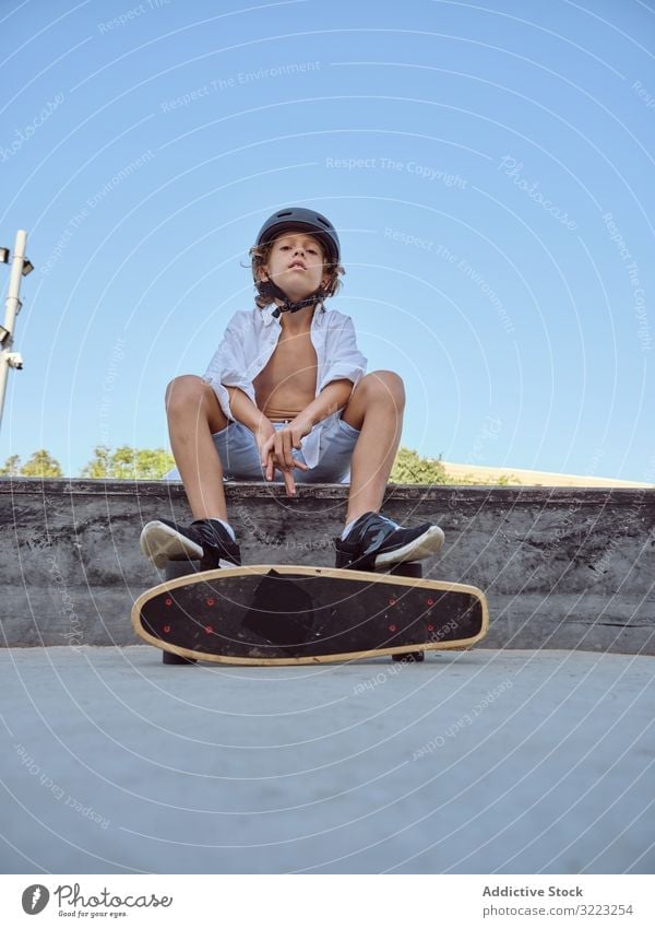 Boy with skateboard sitting on ramp boy skatepark helmet lifestyle sport leisure hobby male young childhood summer sunny careful active fun urban extreme