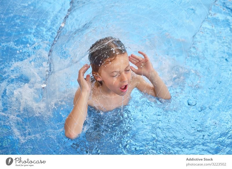 Young boy in blue water swimming pool young child float gasp for air closed eyes open mouth waterfall waterpark activity fun joy health leisure lifestyle
