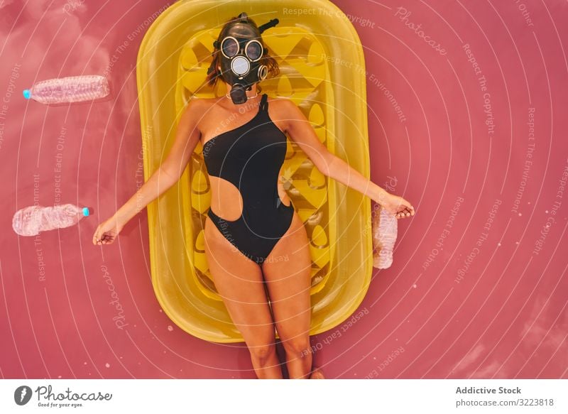 Female in gas mask and with plastic bottles in lake water woman environment sea respirator trash air mattress concept social pink swimsuit red lagoon recycle