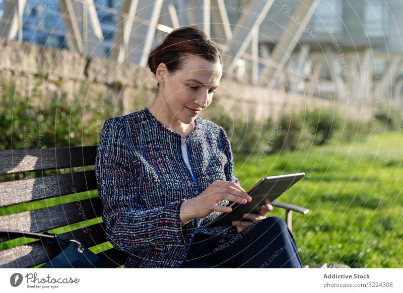 Businesswoman browsing tablet in park businesswoman using serious frown bench sit sunny daytime female city urban work job internet device gadget focused