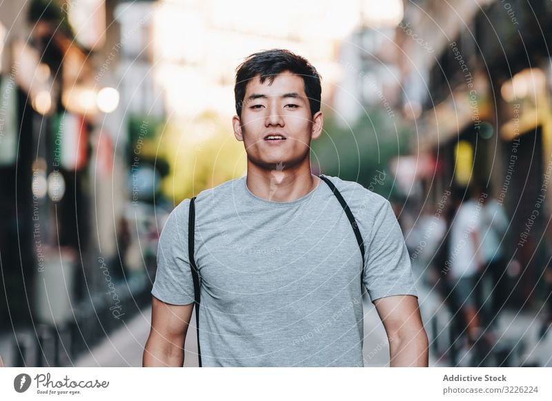 Confident Asian man walking along city street confident content casual t shirt handsome urban stroll modern summer asian ethnic young adult town relaxed