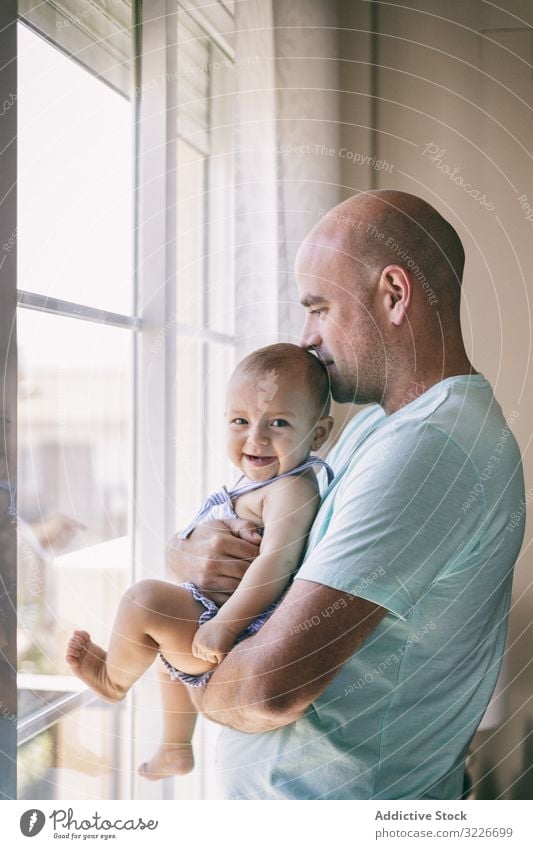 Father with baby looking out window father hug kiss happy cozy home room family man kid child toddler parent together love embrace care cheerful smile carefree