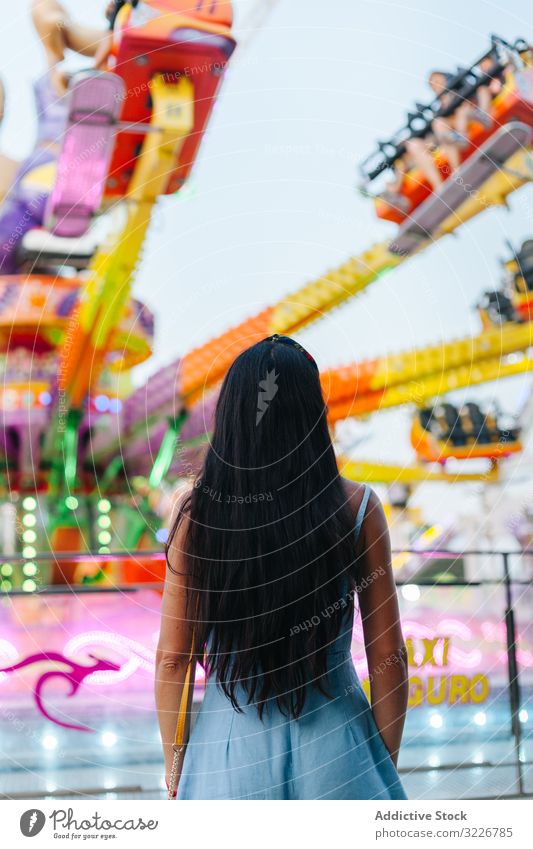 Woman observing spinning carousel at amusement park woman gaze contemplation attraction bright colourful captivating long hair carnival stand fairground summer