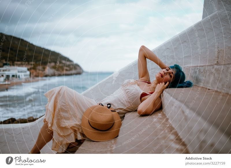Sensual woman in sundress lying on pier stairs sensual step rest coast romantic allure staircase summer freedom seaside seafront beach hat colorful blue hair
