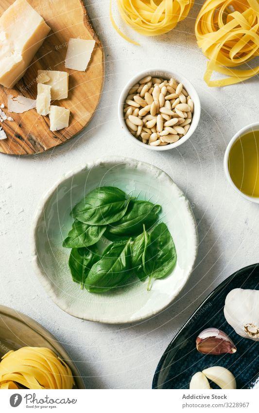 Basil leaves and ingredients for pesto sauce on plates on table basil fresh green colorful herb pine nuts parmesan cheese kitchen pasta arranged leaf white