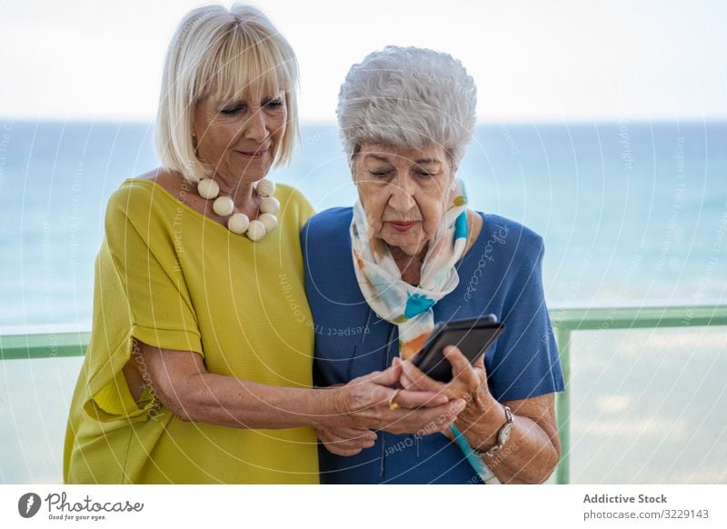 Senior ladies using smartphone on hotel balcony women elderly friend sea resort social media senior mature together friendship device gadget terrace elegant