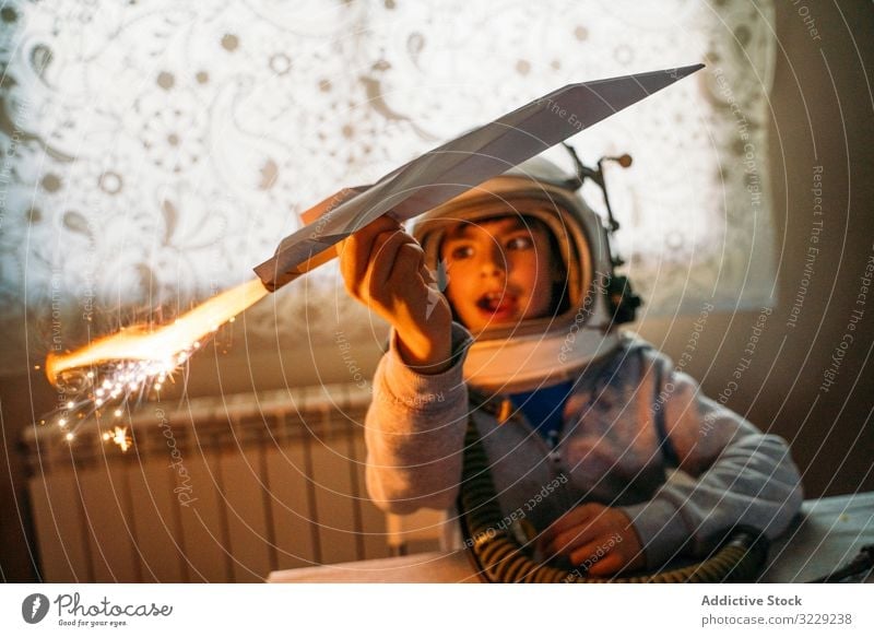 Dreamy kid having fun with toy airplane boy play fantasize paper dreamy astronaut helmet home child happy childhood leisure game joy cute cheerful sit rest