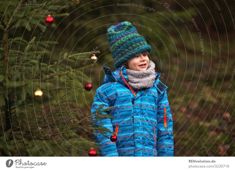 Child stands at a Christmas tree in the forest Front view Upper body portrait Central perspective Shallow depth of field blurriness Day Exterior shot