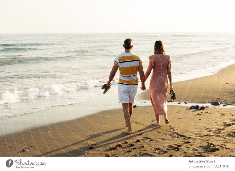 Adult couple walking towards sea beach sand wave resort together holding hands vacation man woman adult barefoot honeymoon weekend water ocean happy holiday