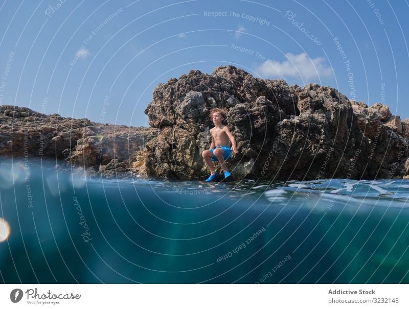 Little kid jumping into sea cliff boy ocean shore active water enjoy summer sky sportive wave motion sunny excited coast rock travel stone vacation child ripple