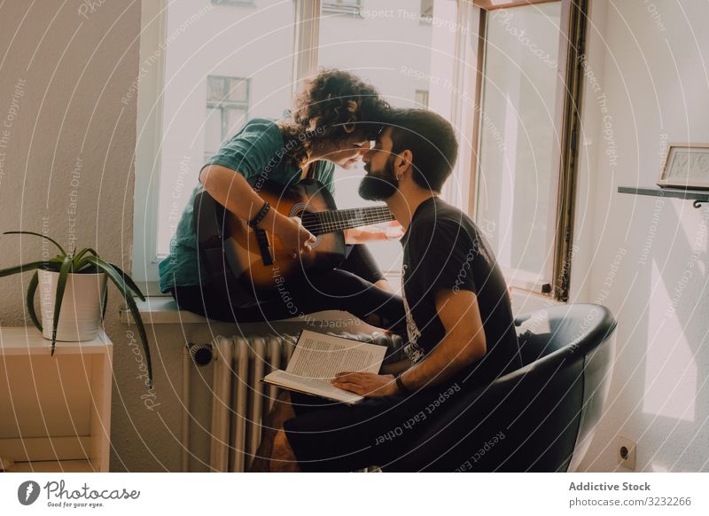 Cheerful couple spending time together at home guitar kissing play book read happy cheerful smile listen hobby pastime passion window modern young adult bonding