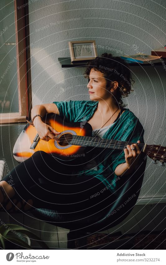 Content woman playing guitar at home content relaxed casual barefoot acoustic minimalistic room floor sit musician guitarist crossed legs young adult leisure