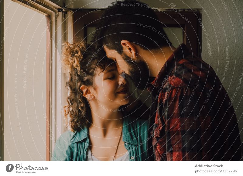 Happy couple embracing on window sill at home embrace happy windowsill joyful smile casual hug hipster modern tender affection lover relationship together