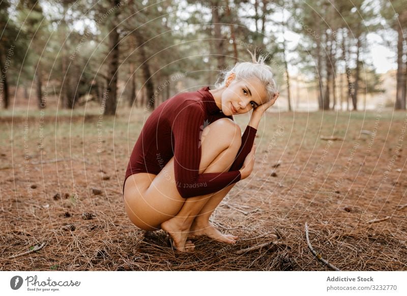 Beautiful modern woman resting barefoot in evergreen forest woods harmony squatting primitive embracing knees blonde carefree attractive beautiful charming
