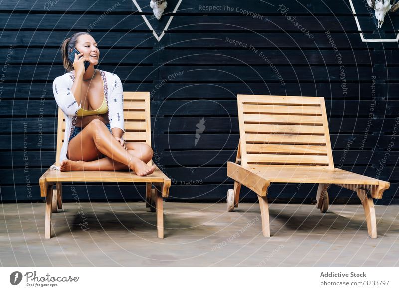 Delighted woman talking on phone while resting on deck chair mobile phone delighted happy smile speak smartphone using sit casual costa rica crossed legs wooden