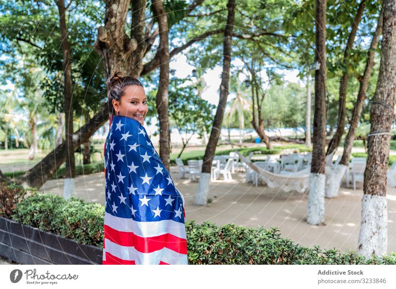 Content woman smiling wrapped in American flag walking along park american flag national content smile cheerful carry cape tree leafy greenery adult young