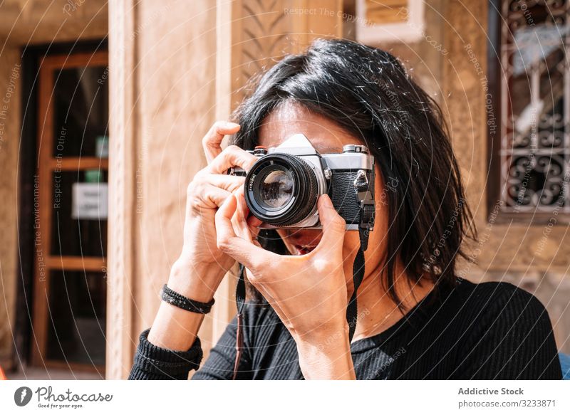 Female photographer taking picture with camera on street woman positive smile casual adjusting using optics cafe young adult photography professional creative