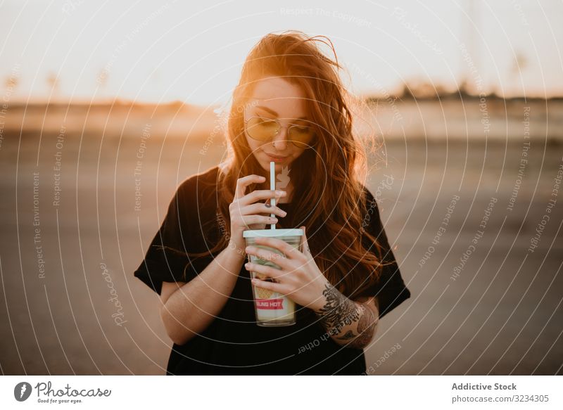 Long haired teenage girl drinking milkshake woman millennial cheerful cool style happy sunset tattoo sunglasses piercing leisure smile straw long haired stylish