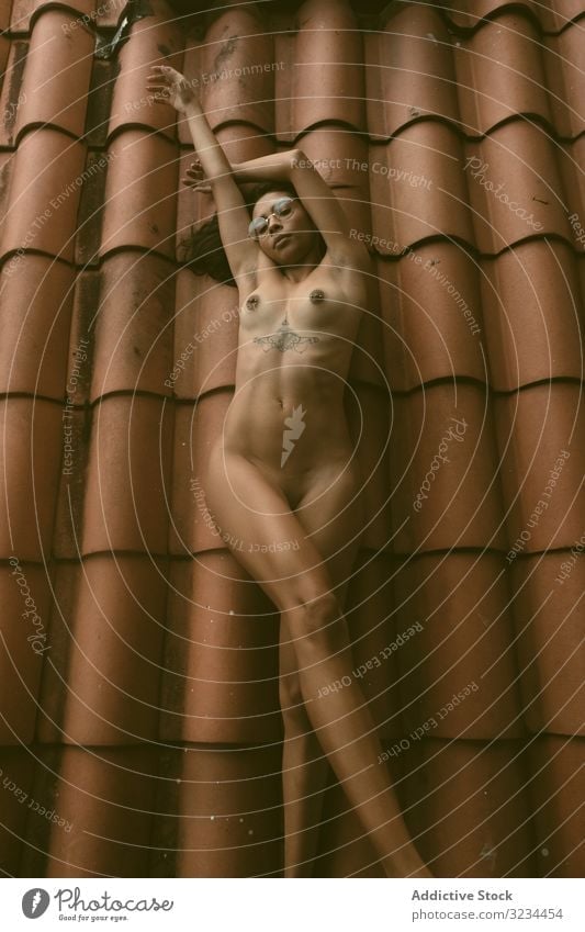 Naked woman lying on roof naked sensual raised arms ethnic tiled house young allure body rest female relax breast brunette lady hands up sexy tattoo call