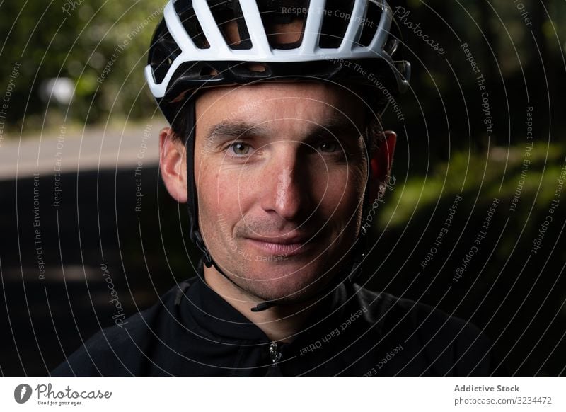 Positive cyclist looking at camera in park training positive man smile helmet sunny daytime sport summer male safety protection glad pleased adult uniform