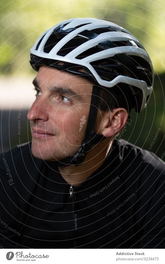 Positive cyclist looking away in park training positive man smile helmet sunny daytime sport summer male safety protection glad pleased adult uniform sportswear