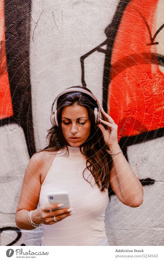 Woman listening to music and using smartphone woman headphones summer graffiti concrete street urban street style grunge social media gadget colorful lifestyle