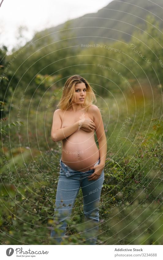 Pregnant topless woman looking away and covering breast while standing in meadow pregnant freedom expectation happy maternity cheerful childbearing belly smile