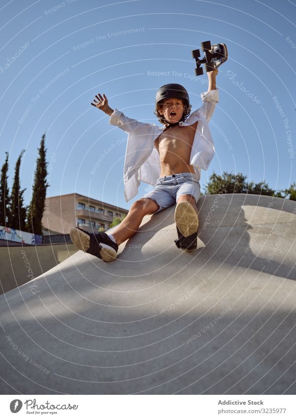 Child on ramp with skateboard in hand child skatepark ride fun helmet trick modern blue sky yell sport leisure hobby ready boy young carefree childhood summer