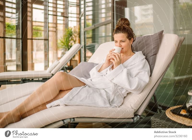 Content female relaxing in wellness center woman spa enjoyment bathrobe chaise lounge drink rest content positive comfortable pensive thoughtful natural