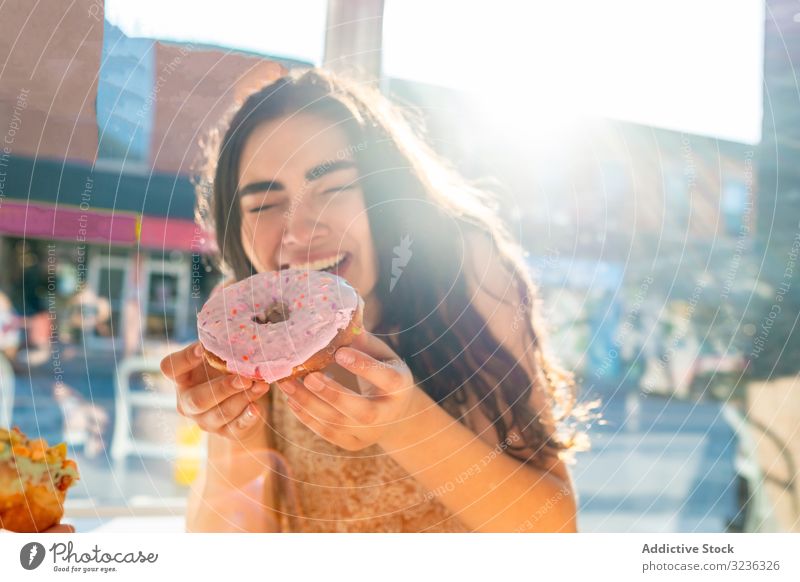 Woman enjoying tasty donut in cafe woman eat bite content delighted pastry glazed round sundress sunny window table sit box young adult sweet dessert lifestyle
