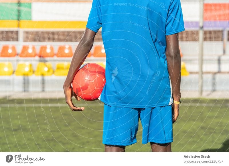 Black football player with ball standing on stadium field training seats sportswear ethnic grass male soccer lawn net sunny daytime black african american