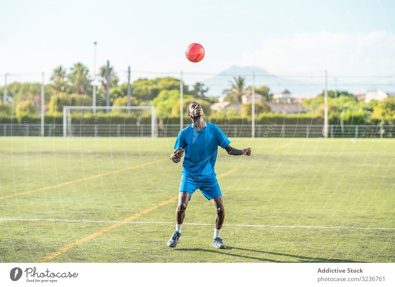 Skinny black teenager jugging football ball on head juggle field training player sportswear ethnic grass male adolescent soccer lawn sunny daytime