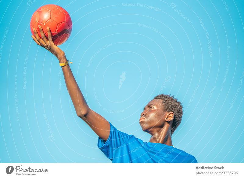 Black teenager with football ball against sky raised arm cloudless training sportswear ethnic holding show male adolescent soccer lawn black african american