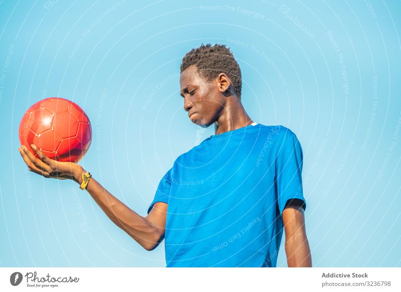 Black teenager with football ball against sky raised arm cloudless training sportswear ethnic holding show male adolescent soccer lawn black african american