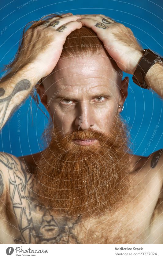 Confident adult red haired hipster touching hair and looking at camera man confident beard mustache thoughtful macho severe serious pensive independent