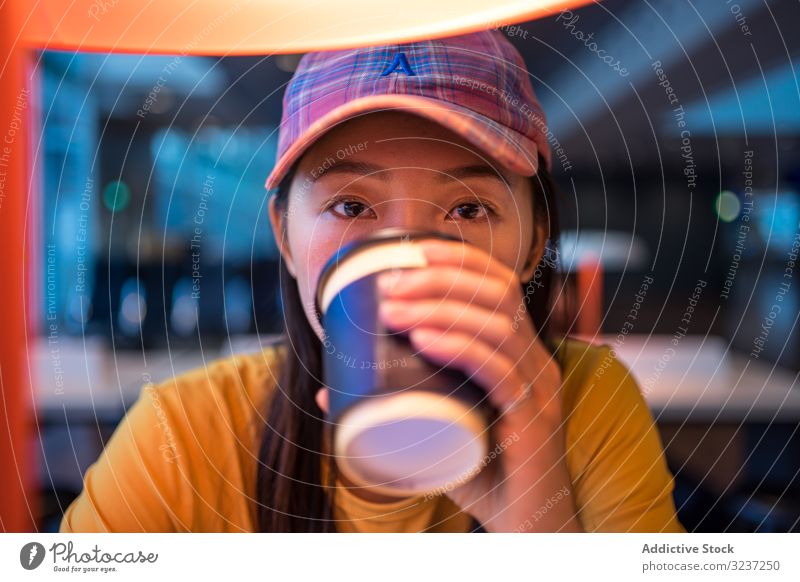 Asian woman drinking coffee at table under lighting lamp airport disposable cup holding female beverage asian takeaway cheerful relaxation hot drink relaxing