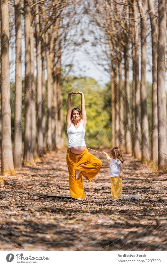 Cheerful mother and daughter practicing yoga in park during sunny day cheerful stretch glade relax fun practice exercise laugh harmony pose pregnant expectation