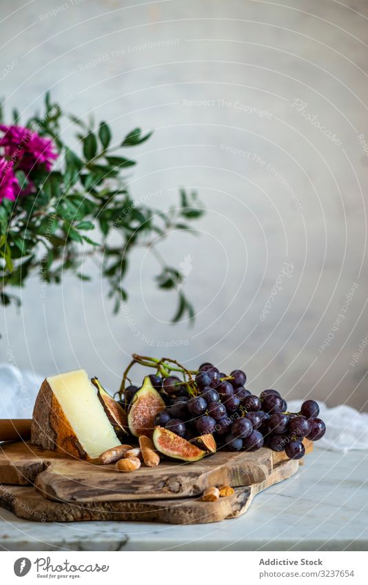 Ripe figs and dark blue grapes next to piece of cheese on cutting boards near pink flowers fresh fruit refreshment slice food tasty nutrition tropical crop meal