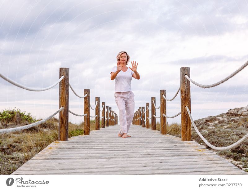 Barefoot lady exercising on wooden path woman breath gesture exercise tai chi closed eyes meditation nature sky cloudy training barefoot female adult healthy