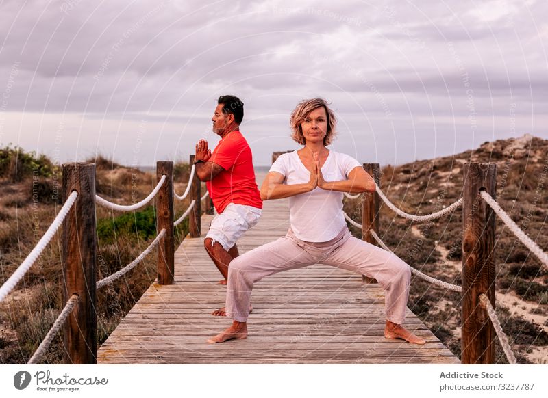 Adult couple meditating on wooden path meditation breath exercise tai chi clasped hands nature sky cloudy training woman adult healthy fit yoga zhineng qigong