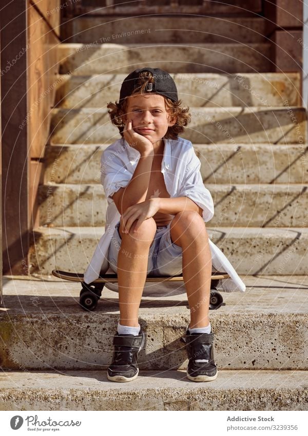 Child sitting on stairs in skatepark boy skateboard style cheerful happy child lifestyle rest leaning on hand sport leisure hobby young childhood summer sunny