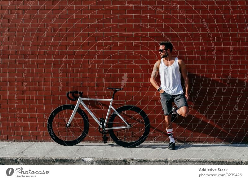 Sportive man standing next to brick wall with bike bicycle rest modern sportive active leaning relax summer male handsome confident sunglasses cyclist athletic