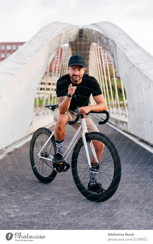 Cheerful man with bicycle standing on footbridge bike city ride modern active sportive summer male adult happy cheerful smile beard cap cyclist healthy