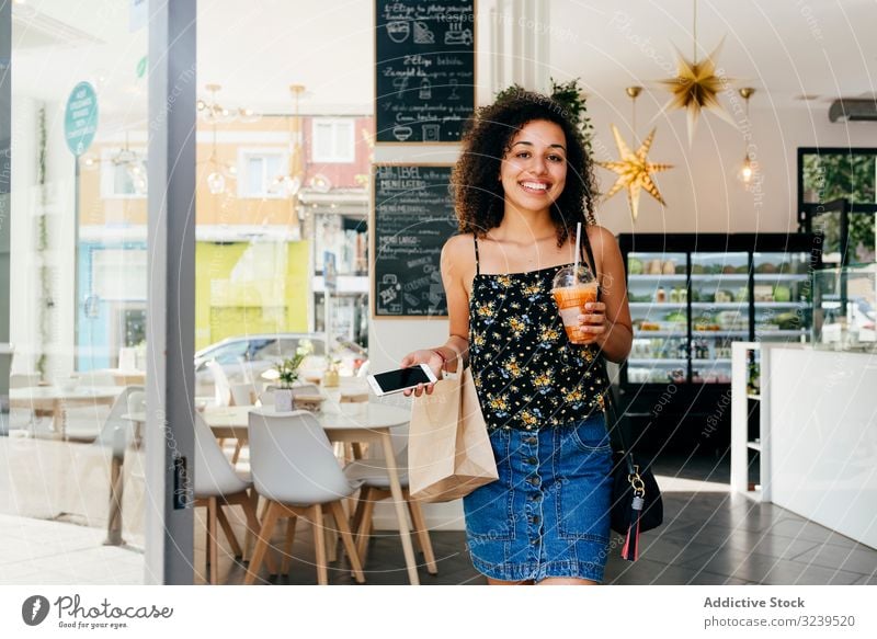 Cheerful ethnic woman leaving restaurant cafe drink healthy smile smartphone paper bag leave female urban vitamin beverage juice smoothie cup detox cheerful
